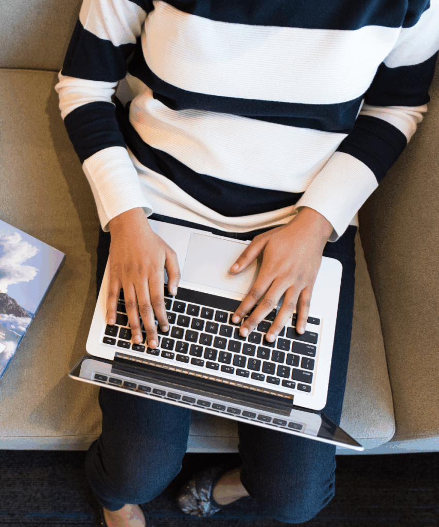 A person in a black and white stripe jumper is sat with a computer on their lap.