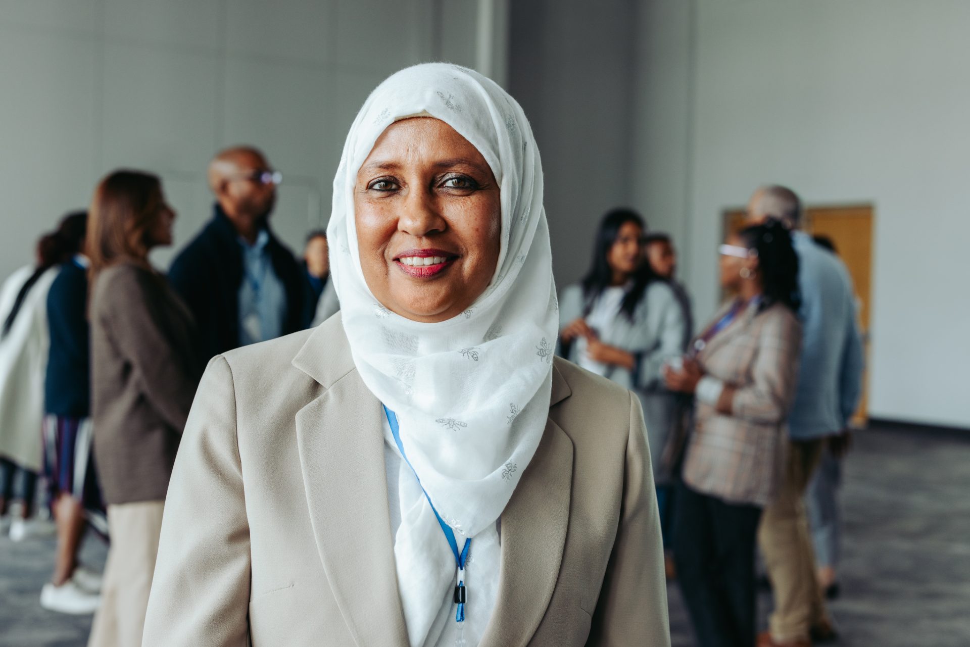 A delegate in a hijab smiling at the camera while colleagues talk behind her
