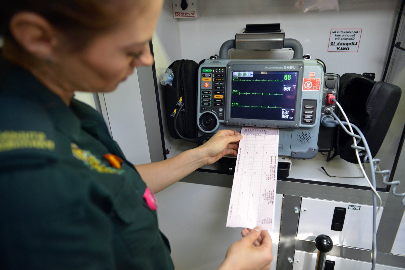 A paramedic reviewing an ECG trace by the monitor in an ambulance