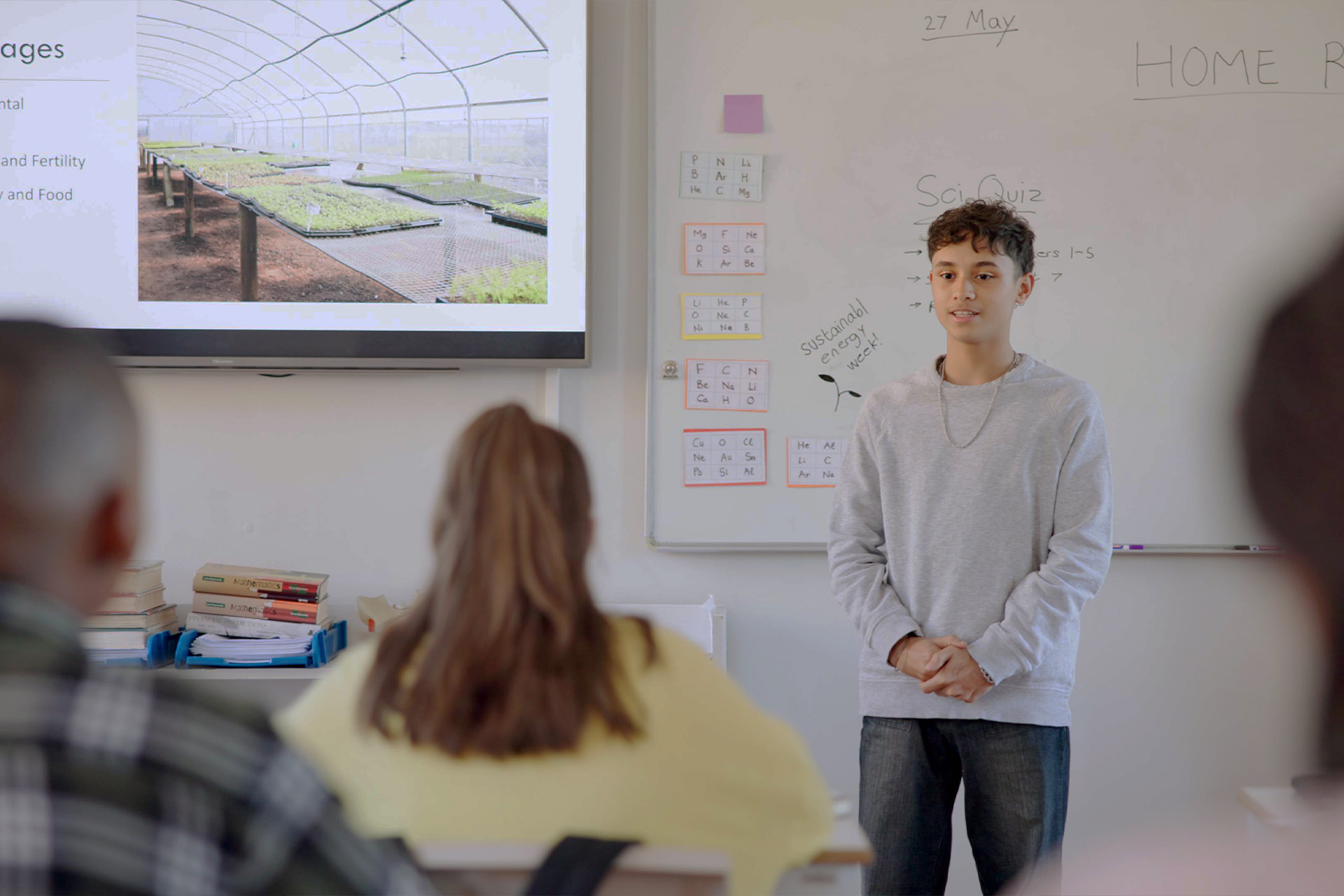 A teenage student standing at the front of a classroom presenting to seated classmates