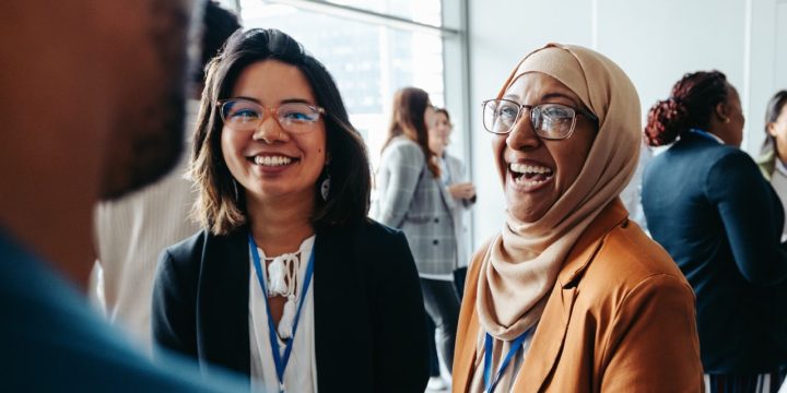 Female colleagues interacting at a corporate workshop, sharing happy smiles and engaging in lively conversations, promoting teamwork and networking in a professional setting.